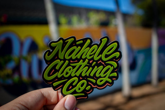 Nāhele Clothing Co. “Concrete Bloom” Sticker - Nāhele Clothing Co. - Nahele Co. - Nahele Clothing Co. - Sticker with 'Nahele Clothing Co.' text held in front of a colorful blurred grafitti style background