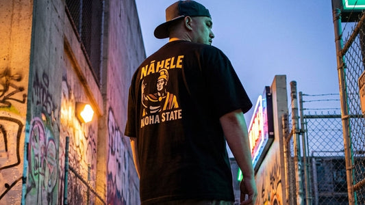 Man wearing a black t-shirt with yellow text standing in an alleyway with graffiti.
